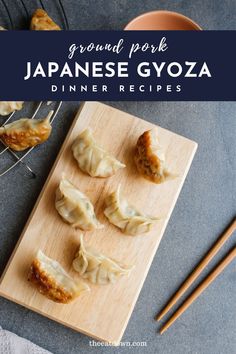 some dumplings are sitting on a cutting board with chopsticks next to them