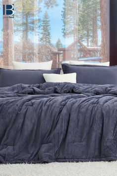 a bed with blue sheets and pillows in front of a window that has snow on the ground