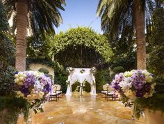 an outdoor wedding ceremony setup with white and purple flowers on the aisle, surrounded by palm trees