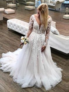 a woman standing in front of a mirror wearing a wedding dress with long sleeves and sheer lace