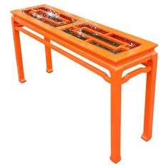 an orange table with two trays sitting on it's legs and the top is made out of glass