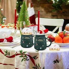 two coffee mugs sitting on top of a table covered in christmas decorations and fruit