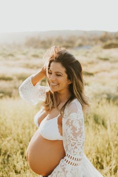 a pregnant woman standing in a field with her hands on her head and looking at the camera