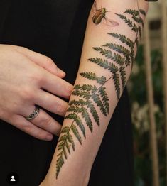 a woman's arm with green leaves and a bug tattoo on the left arm