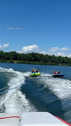 two people on jet skis being pulled by a boat in the water with trees in the background