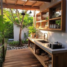 an outdoor kitchen with wooden cabinets and white counter tops, surrounded by plants and trees