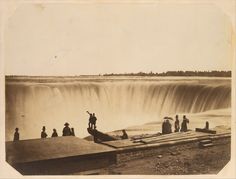 an old black and white photo of people standing at the base of a large waterfall