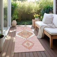 a pink rug on a wooden deck next to a white couch and potted plants