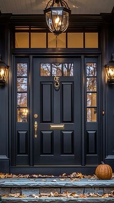 a black front door with two pumpkins on the steps and lights hanging above it