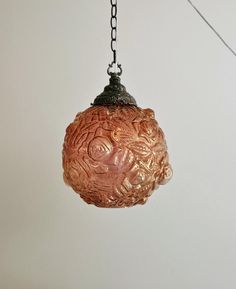 a glass ball hanging from a chain on a white wall with a light fixture in the background