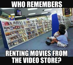 a kid sitting on the floor in front of a book shelf with two people watching movies