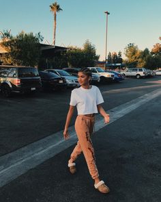 a woman walking across a parking lot in front of parked cars on a sunny day