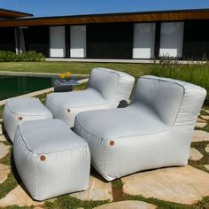 three white lounge chairs sitting on top of a stone walkway next to a pool and grass covered lawn