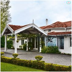 a white house with red tile roofing and green bushes in front of the house