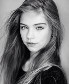 a black and white photo of a young woman with long hair, looking at the camera