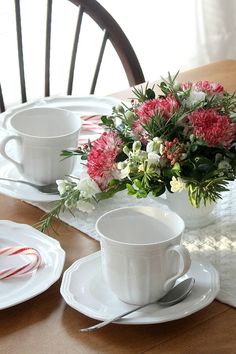 a table set for two with flowers and candy canes in the center, along with plates