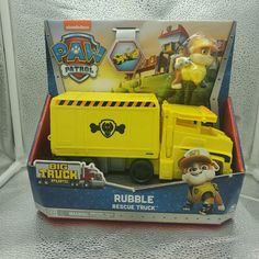 a yellow toy truck in a box on a white surface with other toys behind it