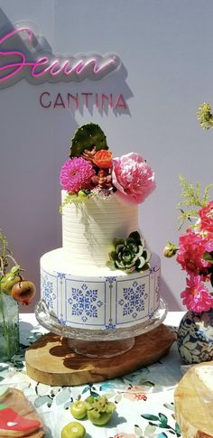 a white and blue cake sitting on top of a table next to vases filled with flowers