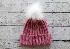 a pink knitted hat with a white pom - pom on the top