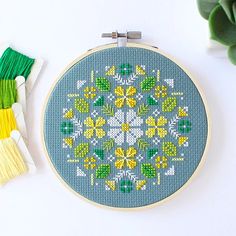 a cross - stitch pattern is shown next to some yarns and scissors on a white surface