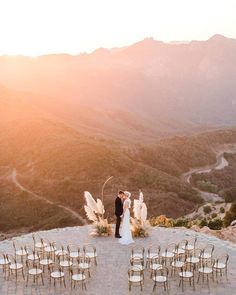 a bride and groom standing at the top of a hill with chairs set up for their wedding ceremony