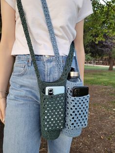 a woman is holding two cell phones in her hand while wearing a crocheted bag