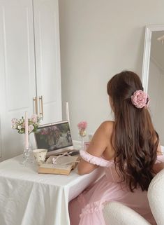 a woman in a pink dress sitting at a table with a book and flowers on it