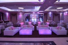 a room filled with white couches and tables covered in purple lighting under chandeliers