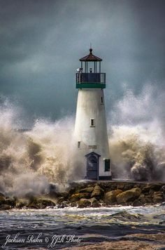 a lighthouse surrounded by waves in the middle of the ocean with dark clouds above it