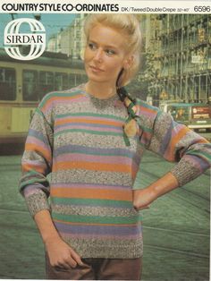 a woman is wearing a colorful sweater and has her hands on her hips while standing in front of a building