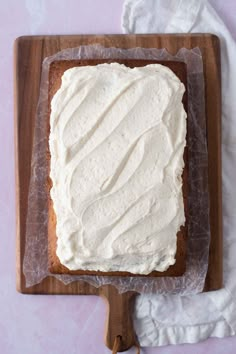 a cake with white frosting sitting on top of a wooden cutting board