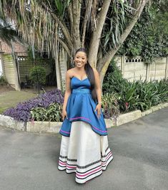 a woman standing in front of a tree wearing a blue and white dress with pink trim