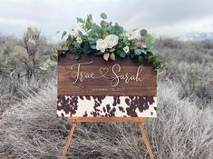 a wooden sign with flowers and greenery on it in the middle of a field