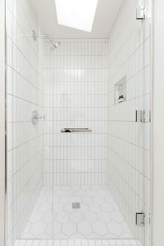 a white tiled bathroom with skylight above the shower stall and tile flooring on the walls