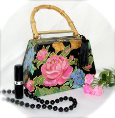 This petite, elegant, one-of-a-kind wooden purse is handpainted in the style of cloissonne, with rich shimmery colors outlined in raised metallic gold. Pink roses, blue hydrangeas and golden trumpet vines cover the black ground, and a satin acrylic varnish seals the design and makes it easy to wipe clean. A natural bamboo handle is draped with a black silky tassel. A small brass latch secures the  closing.  Inside is fully lined with padded fuschia satin, trimmed in gold braid. There's room for Trumpet Vines, Wooden Purse, Roses Blue, Trumpet Vine, Black Ground, Blue Hydrangeas, Bamboo Handles, Blue Hydrangea, Part 4