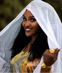 a woman with long hair wearing a white veil over her head and smiling at the camera