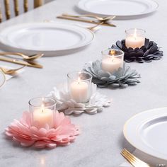 three candles sitting on top of a table with white plates and gold forks next to them