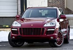 a red porsche cayen is parked in front of a brick building with snow on the ground