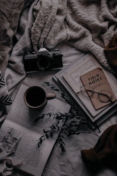 an open book, coffee cup and eyeglasses are on a bed with blankets