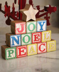 wooden blocks spelling joy noel peace in front of a christmas tree