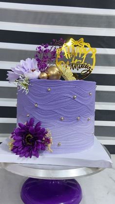 there is a purple cake with gold decorations on the top and flowers in the middle