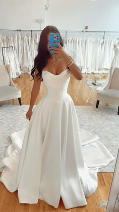 a woman taking a selfie in front of a mirror wearing a white wedding dress