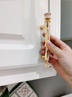 a person is holding onto a door handle in front of a white cabinet with gold trim