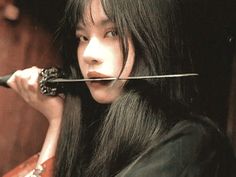 a woman with long black hair holding a knife in her mouth