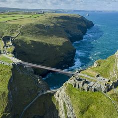 an aerial view of a bridge over the ocean with cliffs on either side and water in the background