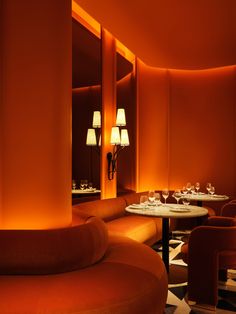 a dimly lit restaurant with orange walls and round tables, two lamps on either side of the table