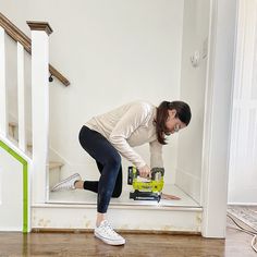 a woman in white shirt and black leggings holding a driller on the floor