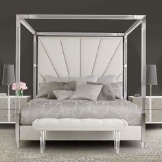 a white bed sitting in a bedroom next to two nightstands and a vase with flowers