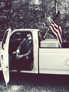 a man sitting in the back of a white truck with an american flag on it