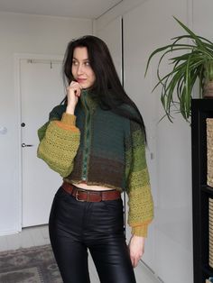 a woman in black pants and a green sweater posing with her hand on her chin